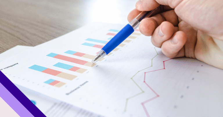 mão de uma pessoa branca segurando uma caneta acima de alguns papéis com gráficos