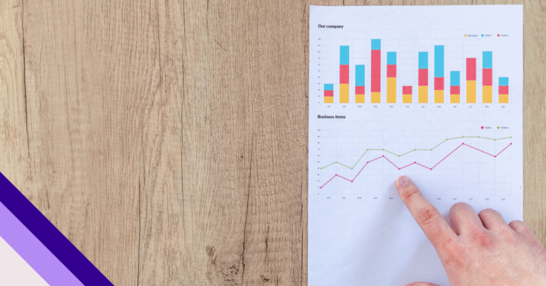 sobre uma mesa de maderia clara um pessoa com mão branca aponta um folha com gráficos de análise de dados de seo local